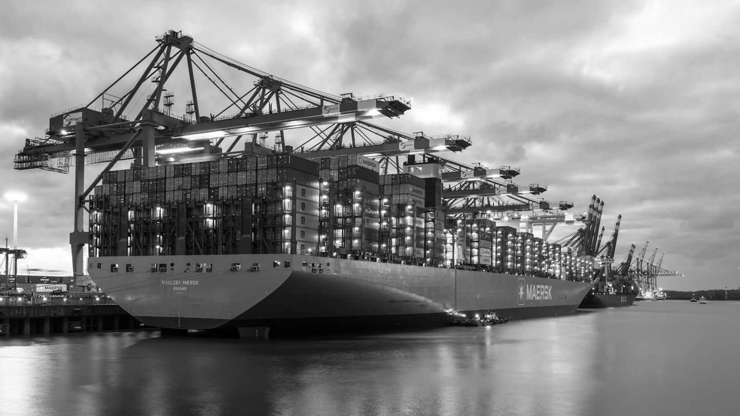 Container ship being loaded by gantry cranes at a busy port at night.