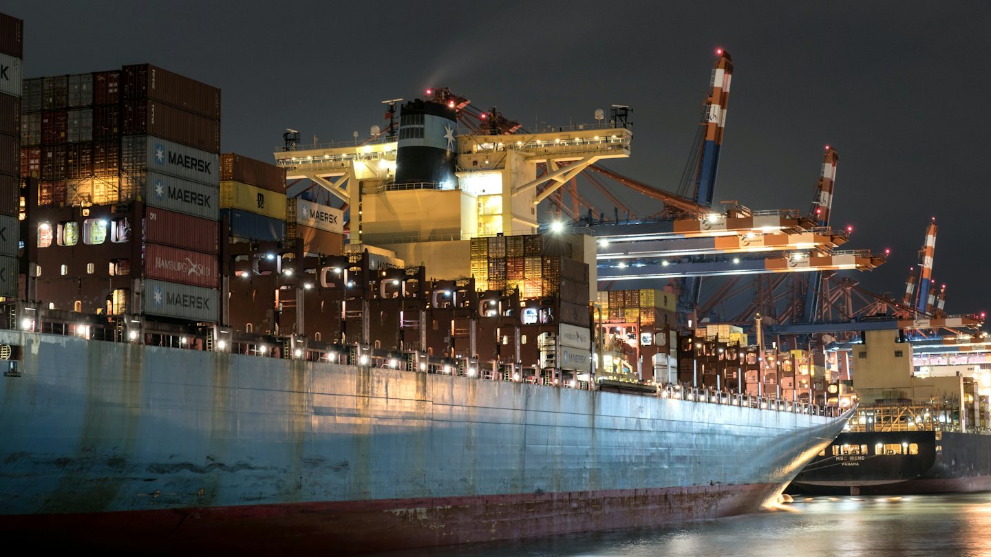 Container ship docked at a port with bright lights at night.