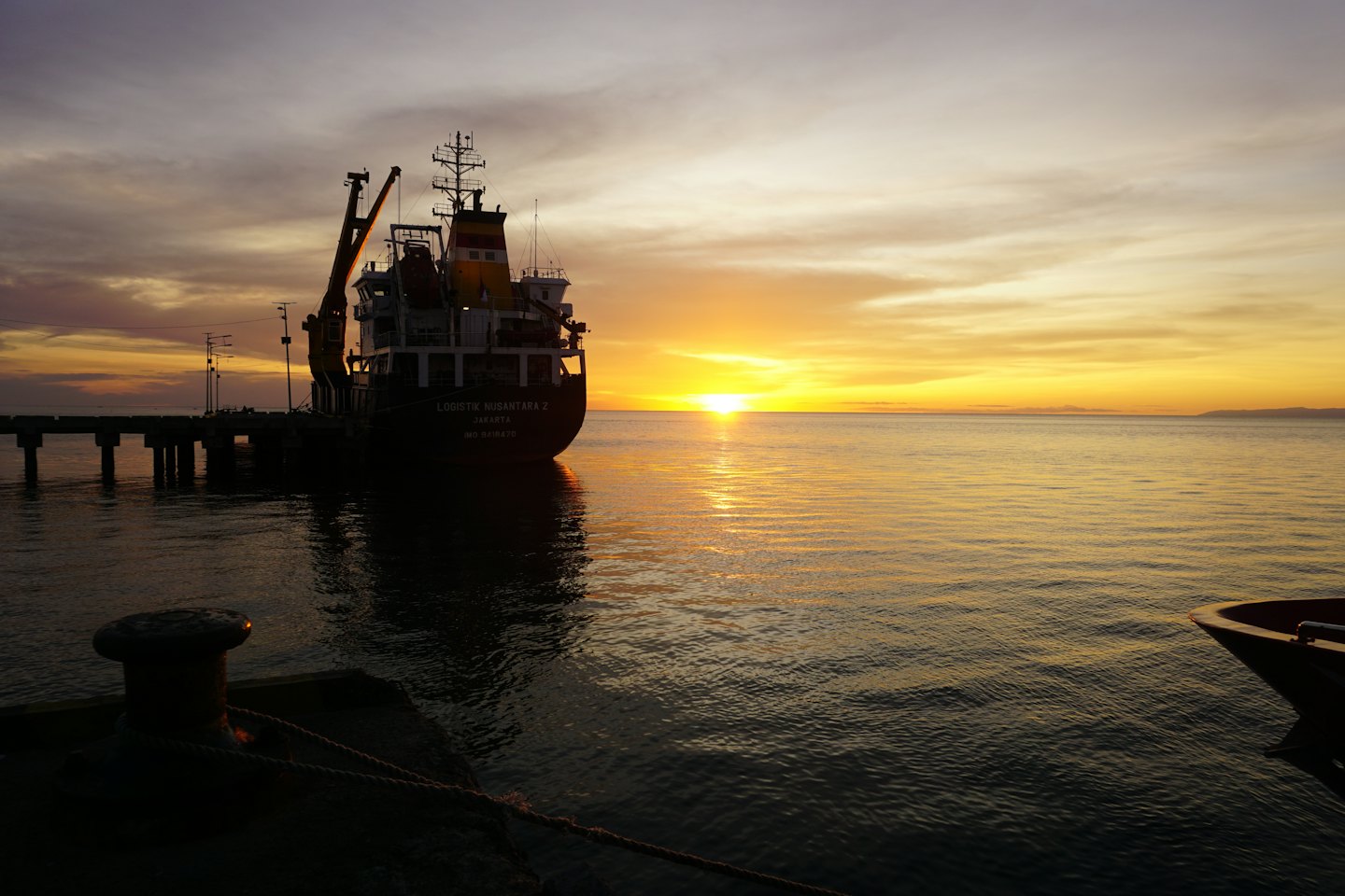 A cargo ship docked at a pier at sunset.