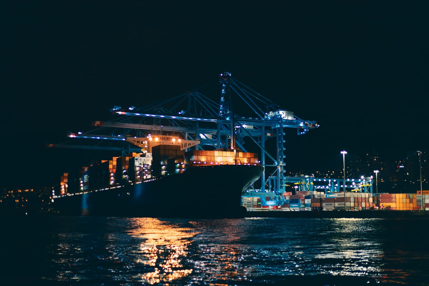 A large cargo ship being loaded by gantry cranes at night.
